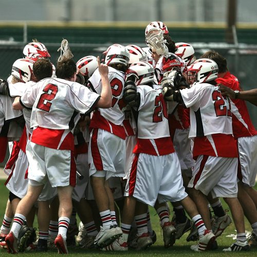 A group of lacrosse players and their coach celebrating a victory on the field.